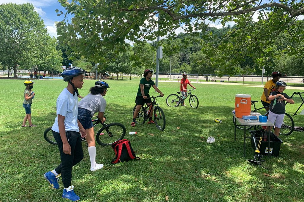 group of students on bikes congregate around a water cooler while social distancing in Asheville