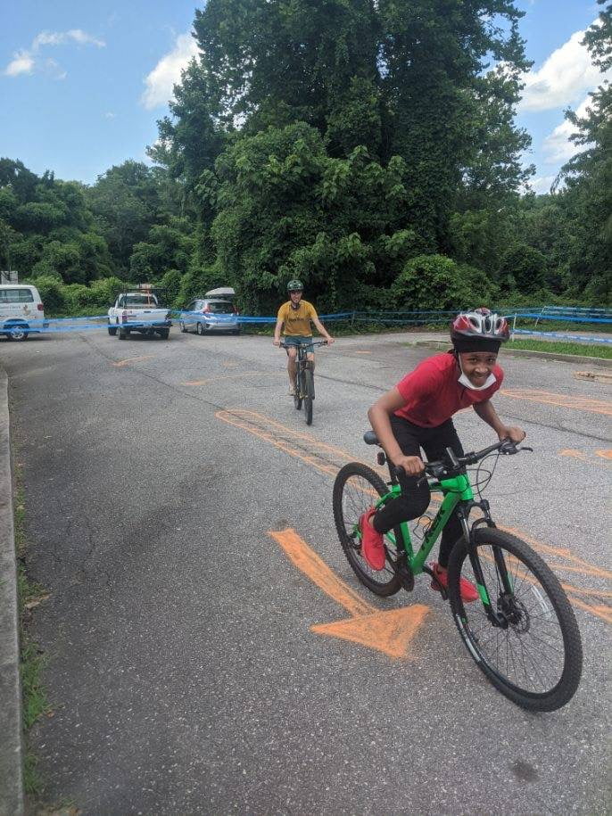 Teen on bicycle pedals past orange arrow written in chalk to delineate temporary bike playground in Asheville